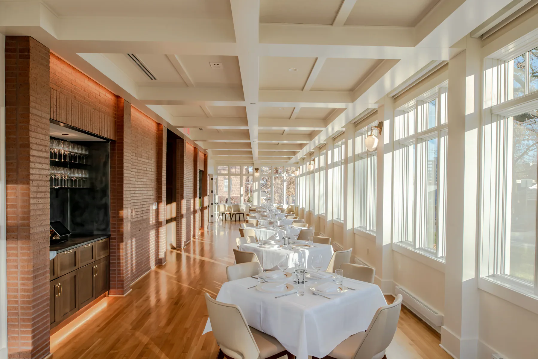 Sunlit restaurant dining room with brick walls and floor-to-ceiling windows